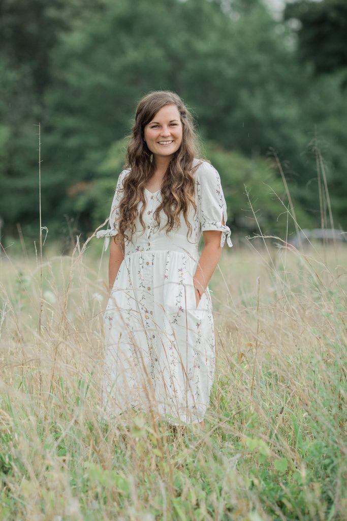 girl standing in the field with white dress and hands in pockets