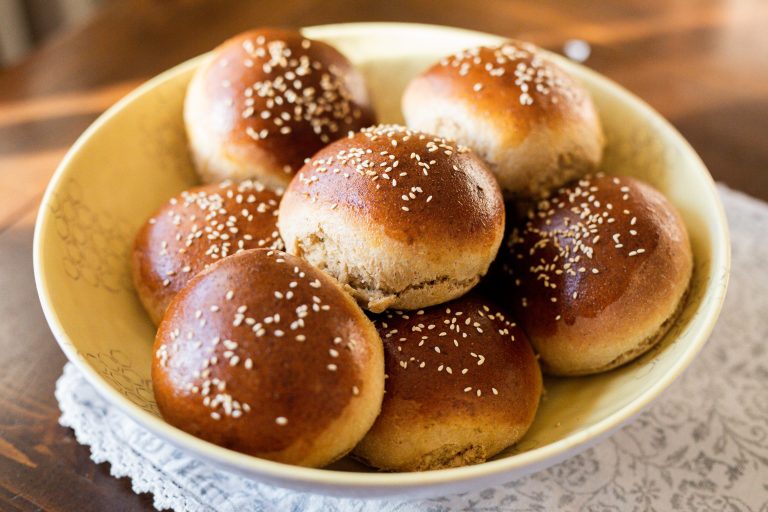 hamburger buns with sesame seeds stacked in a yellow bowl